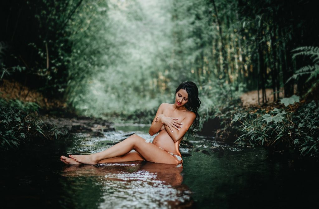 Photo tirée d'une séance photo grossesse in the water en extérieur. Future maman assise dans l'eau de la rivière entourée de bambou à Brest